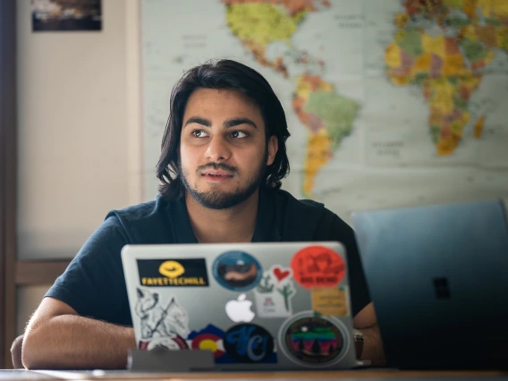 male student with laptop in front of him and a map of the world behind him